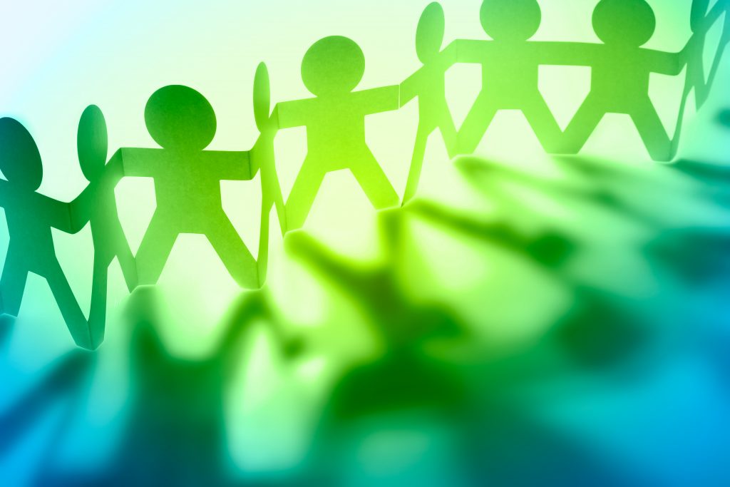 Abstrakte grüne Papierfiguren von Menschen, die sich an den Händen halten.